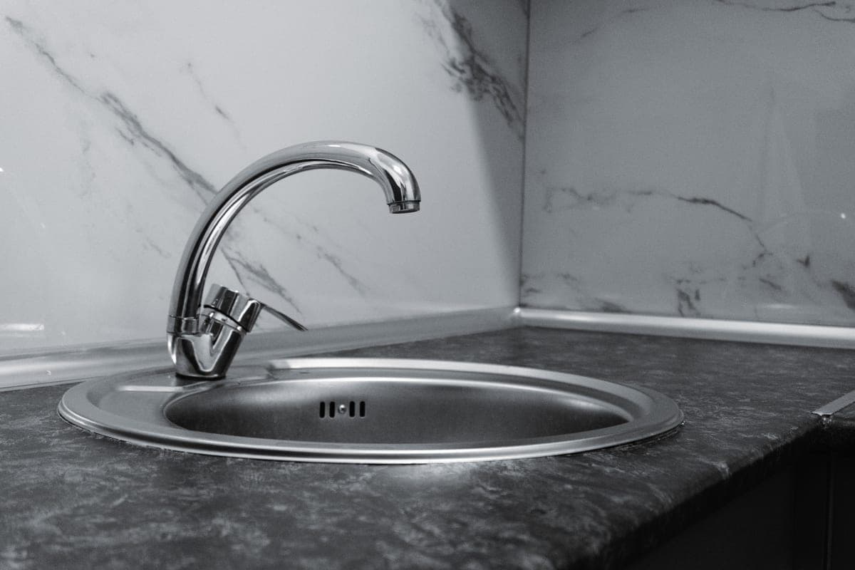 Stainless steel kitchen faucet arcing over a clean sink basin