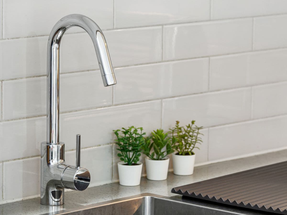 Chrome kitchen faucet over a sink against a tiled backsplash