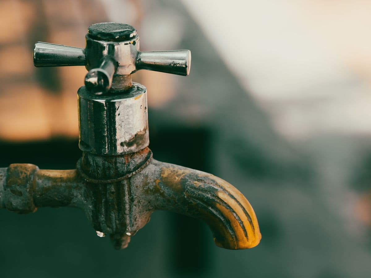 Close-up of a worn metal faucet with water droplets on the spout