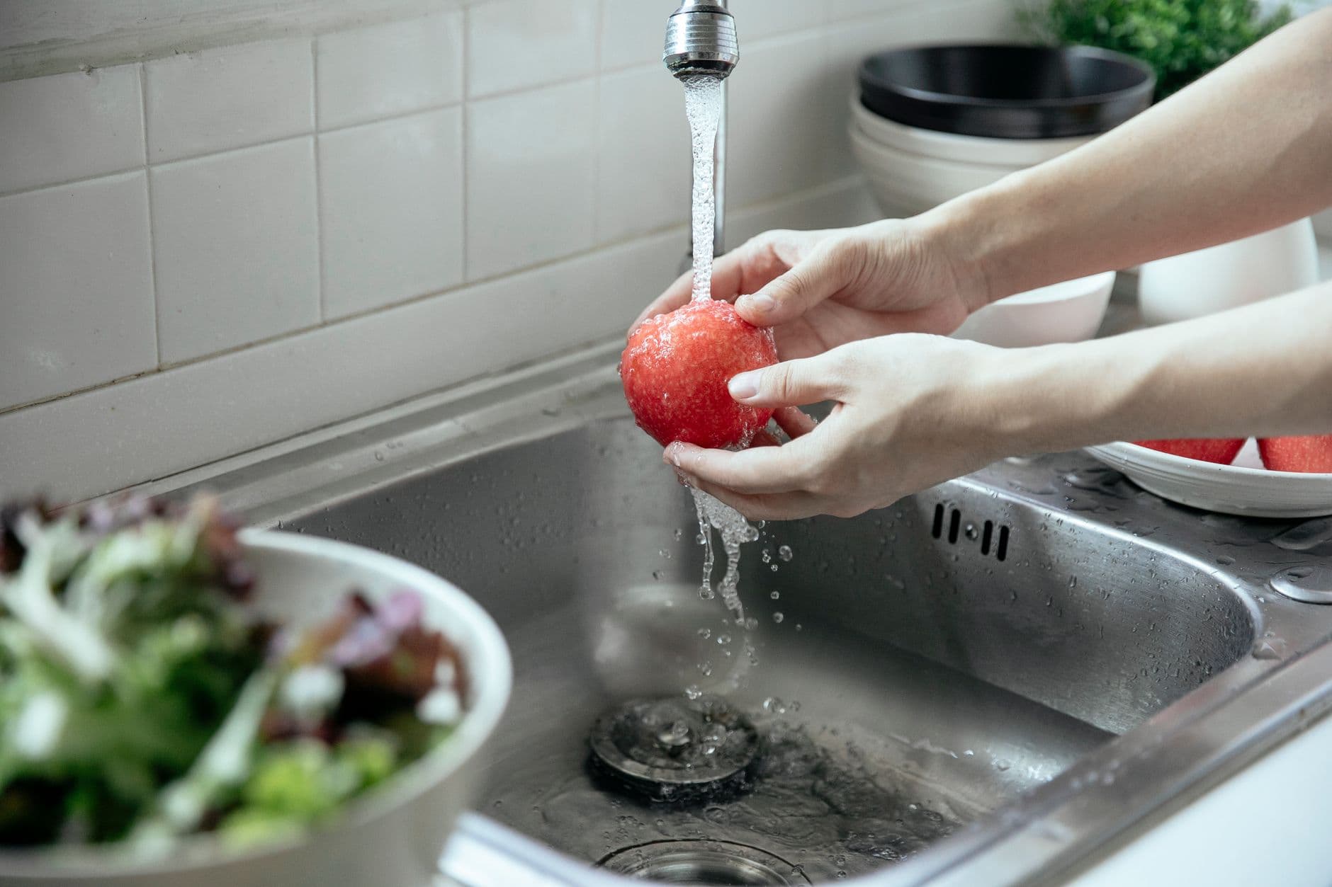 Hands rinsing an apple under running water at a kitchen faucet