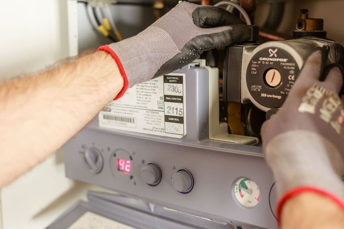 Person working on pipework inside a kitchen base cabinet