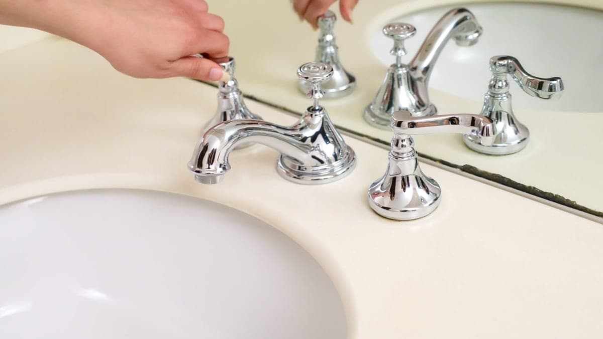 Hands working on drain plumbing beneath a kitchen sink
