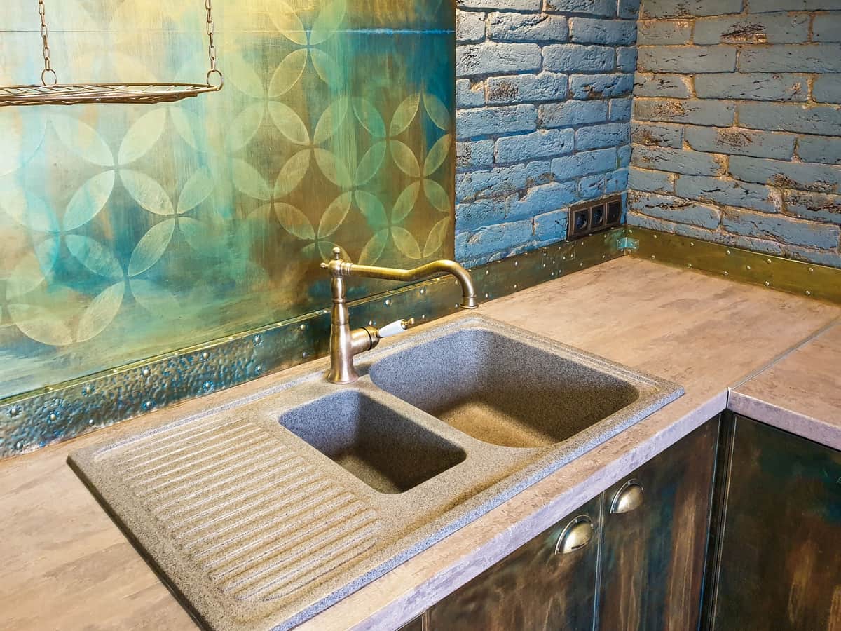 Modern kitchen sink set into a stone countertop with a faucet behind