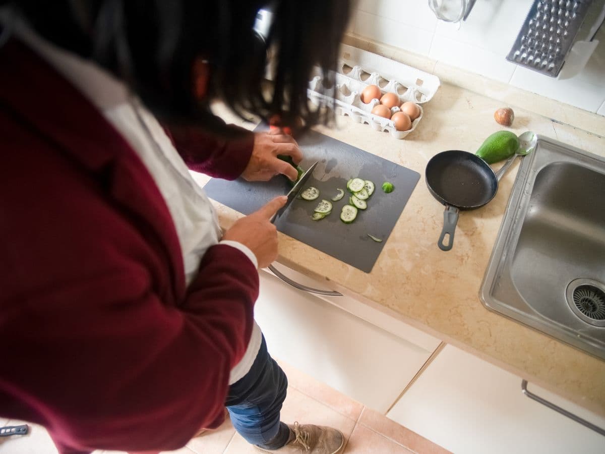 Cook slicing vegetables on a board resting across a kitchen sink