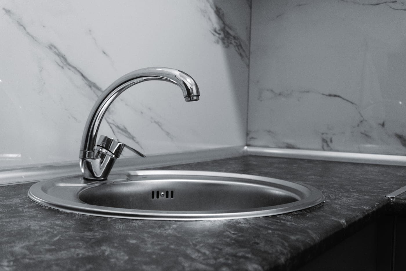 Stainless steel kitchen sink basin with water beading on the base