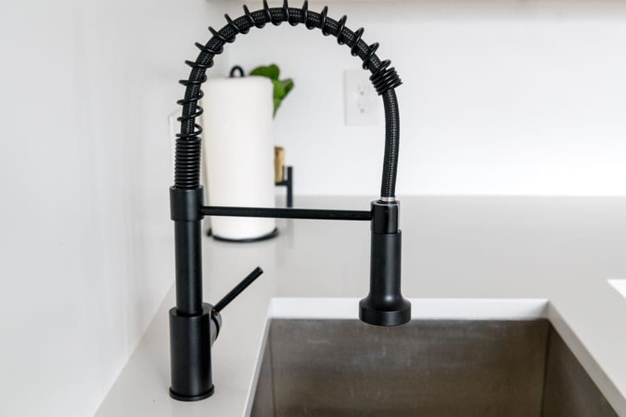 Pull-out kitchen faucet spray head drawn forward from a low spout