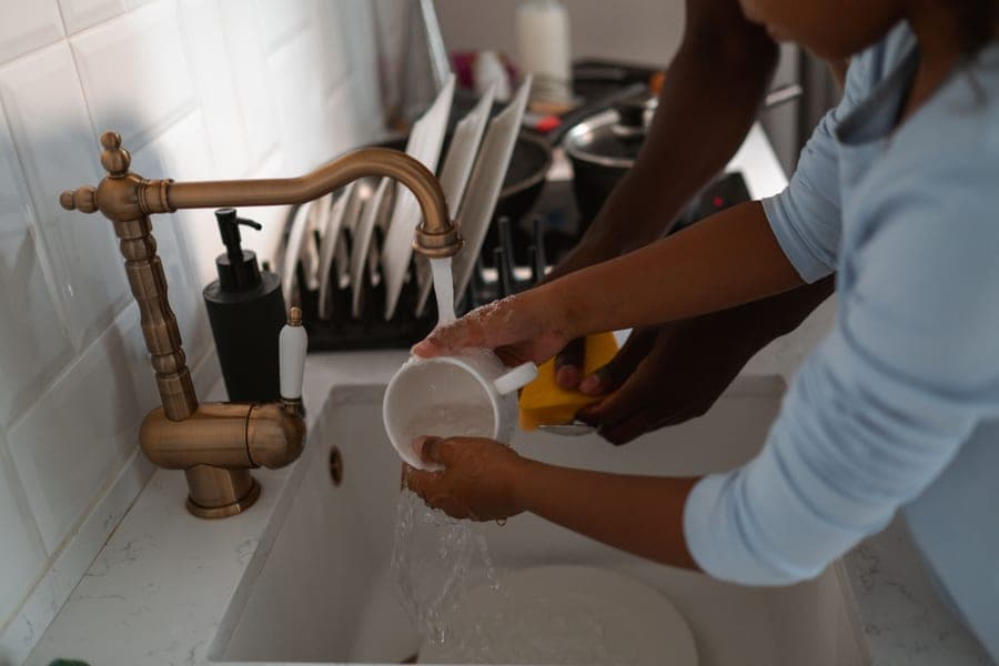An adult and a child washing dishes together at a kitchen sink